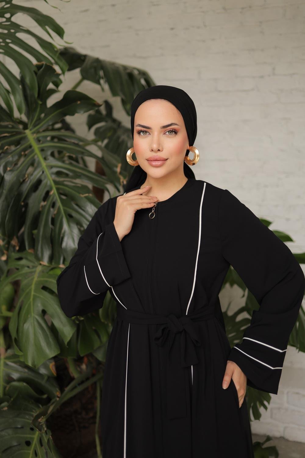 Close up Chic black abaya featuring white contrast piping, a front zipper closure, side pockets, and matching waist belt for a flattering fit.