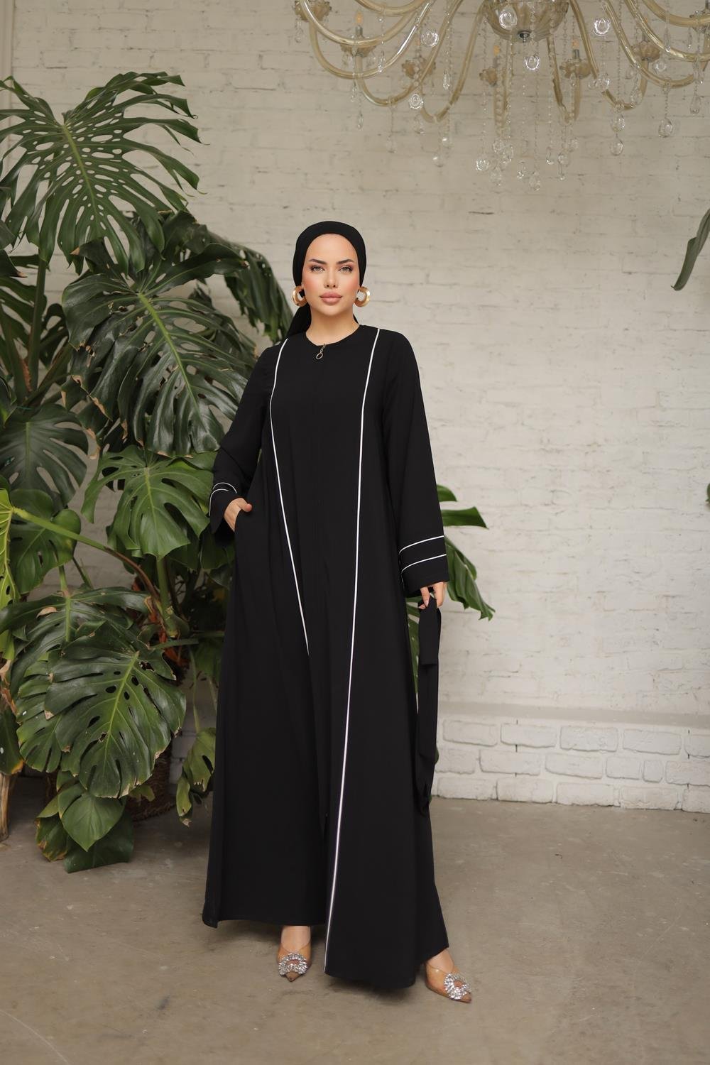 Chic black abaya featuring white contrast piping, a front zipper closure, side pockets, and matching waist belt for a flattering fit.