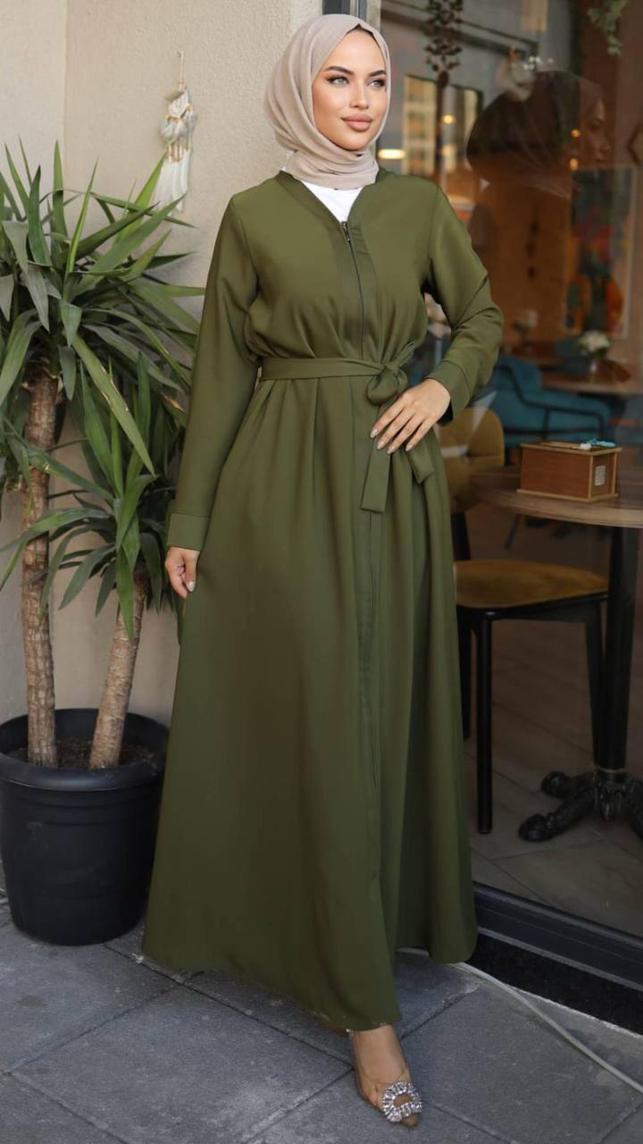 Woman wearing a black zippered abaya with a waist belt.The abaya has a flowy design and long sleeves, paired with a matching hijab and embellished heels.