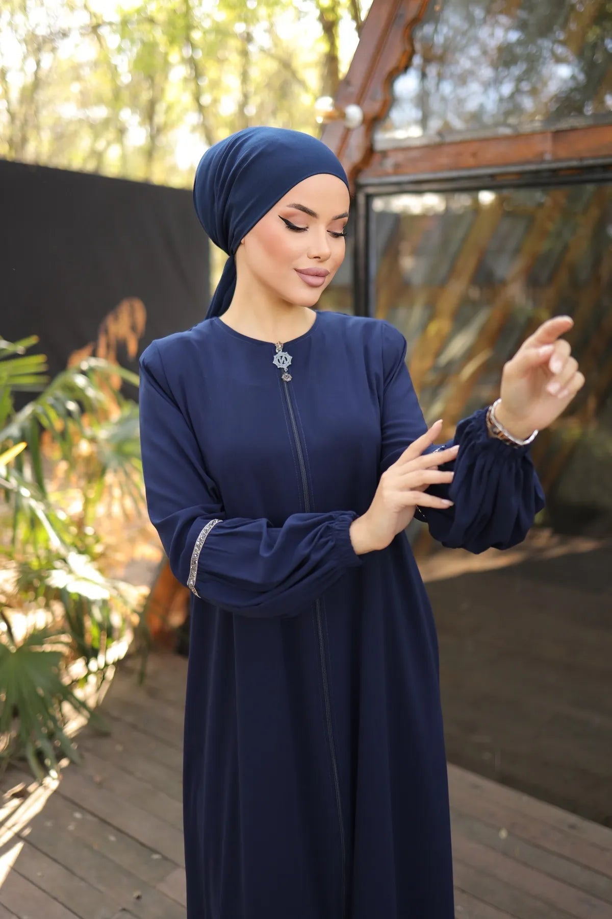 Close up A woman wearing a zipper-front abaya with elegant puff sleeves, a flowing silhouette, side pockets, and a modest fit, paired with a matching hijab and embellished flats.