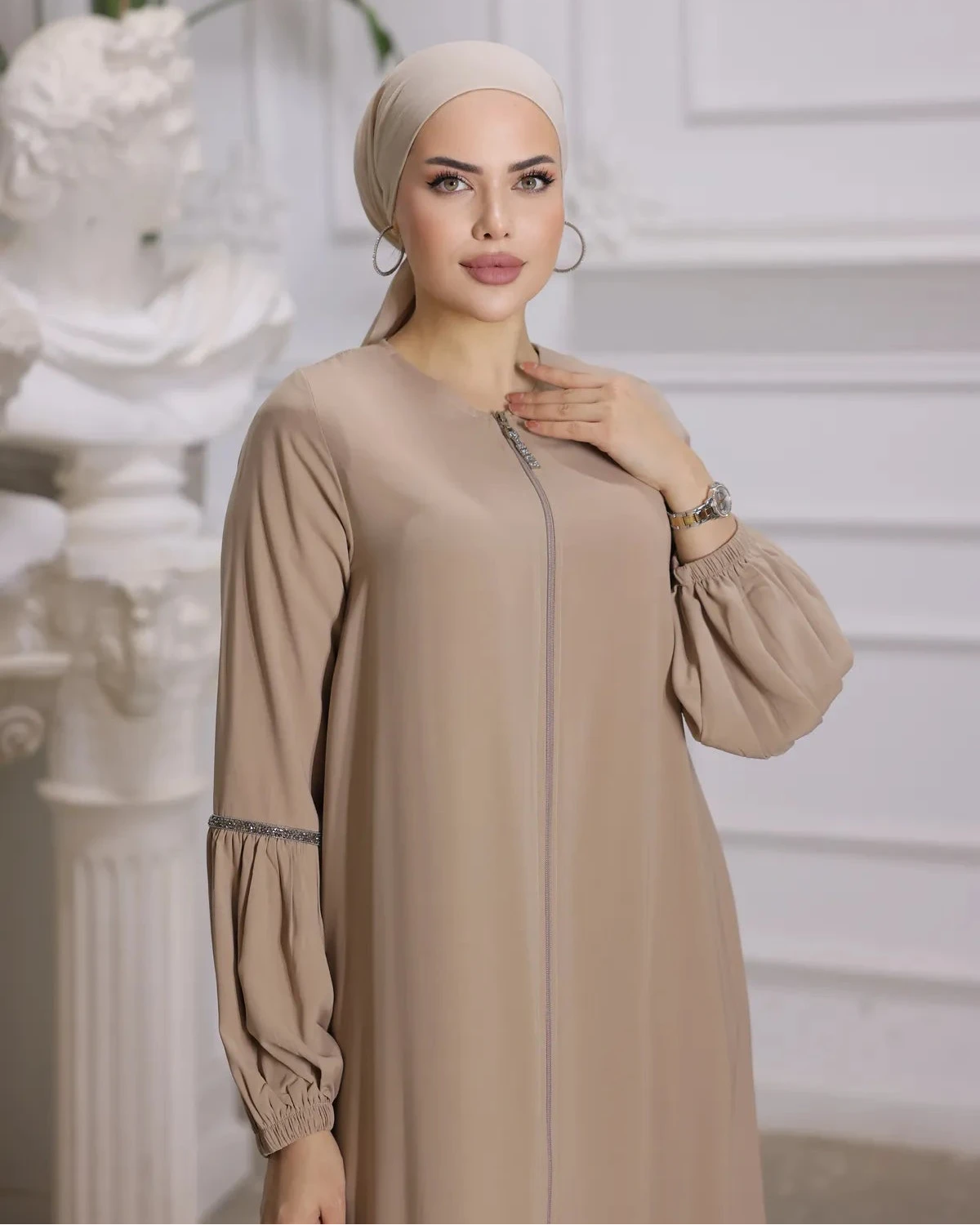 woman wearing a zipper-front abaya with elegant puff sleeves, a flowing silhouette, side pockets, and a modest fit, paired with a matching hijab and embellished flats.
