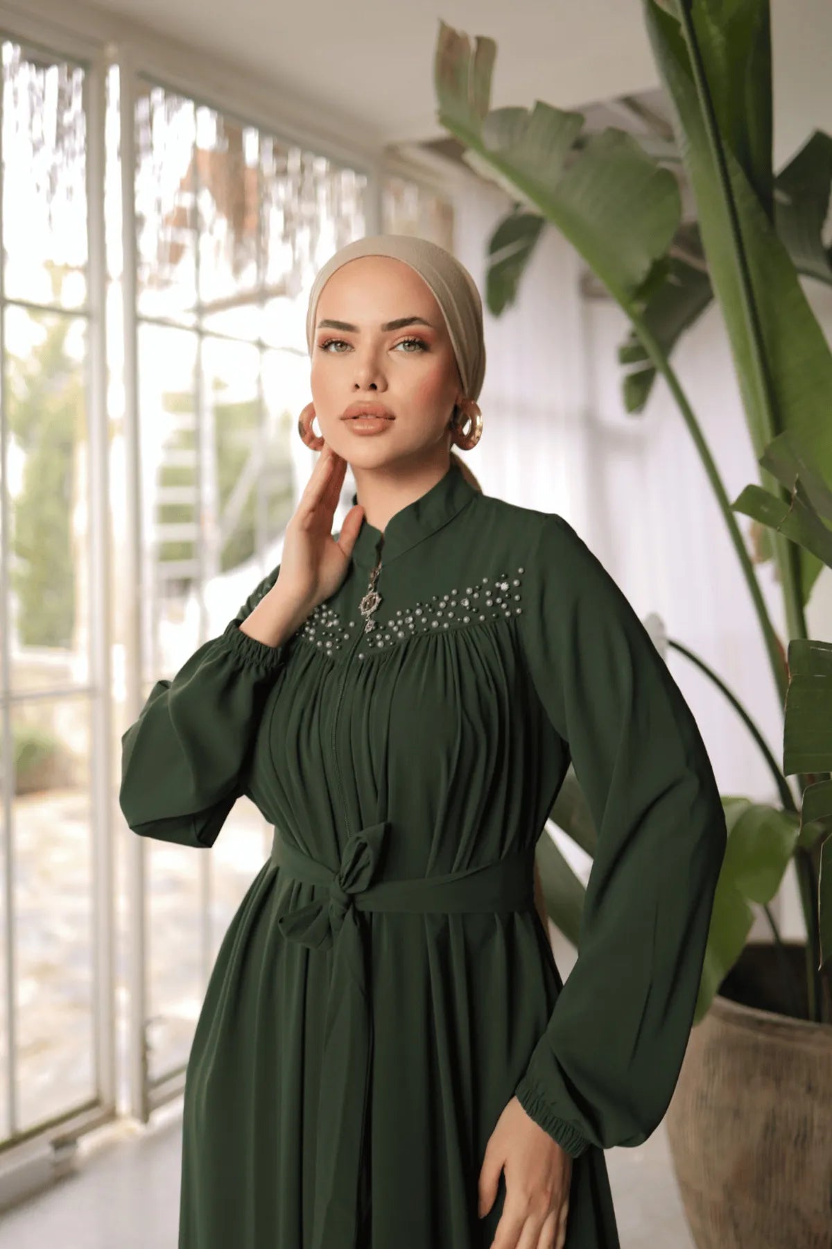 Chic green abaya featuring side pockets, a front zipper closure, and matching waist belt for a flattering fit. Embellished with pearls on the upper chest.