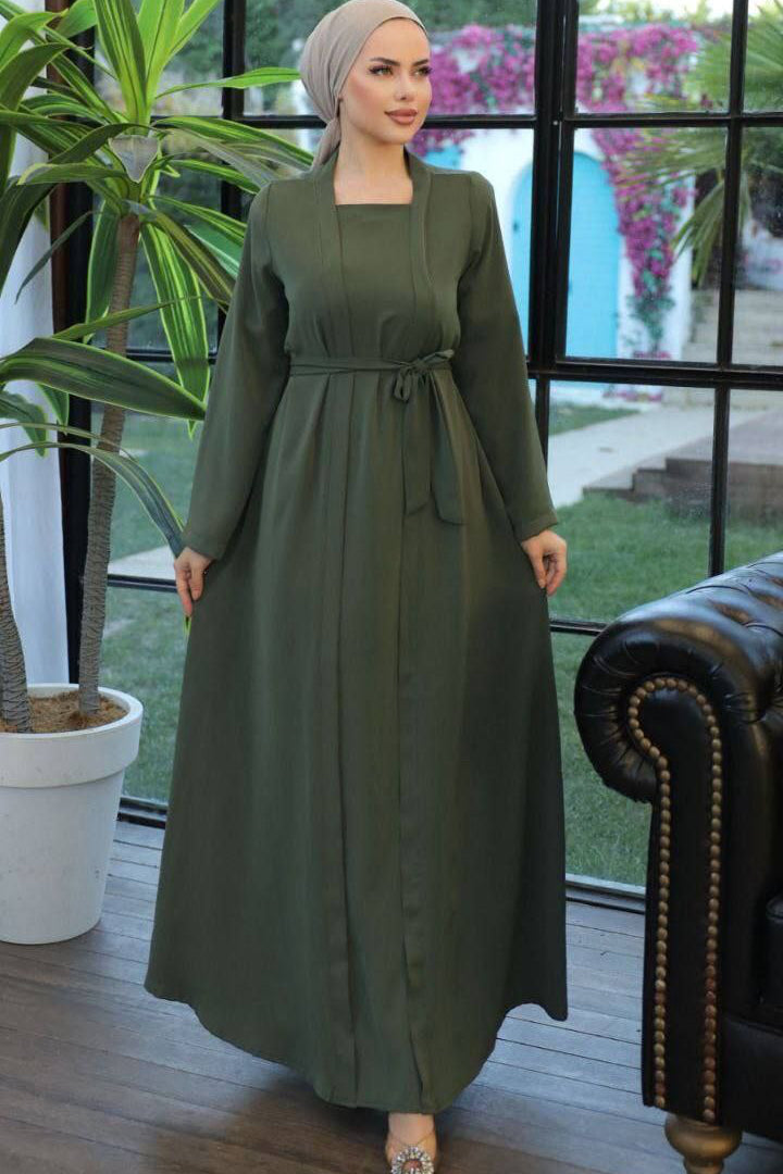 A woman wearing a one-piece kimono-style abaya with a matching belt, long wide sleeves, and a modest silhouette, paired with a hijab and embellished flats.