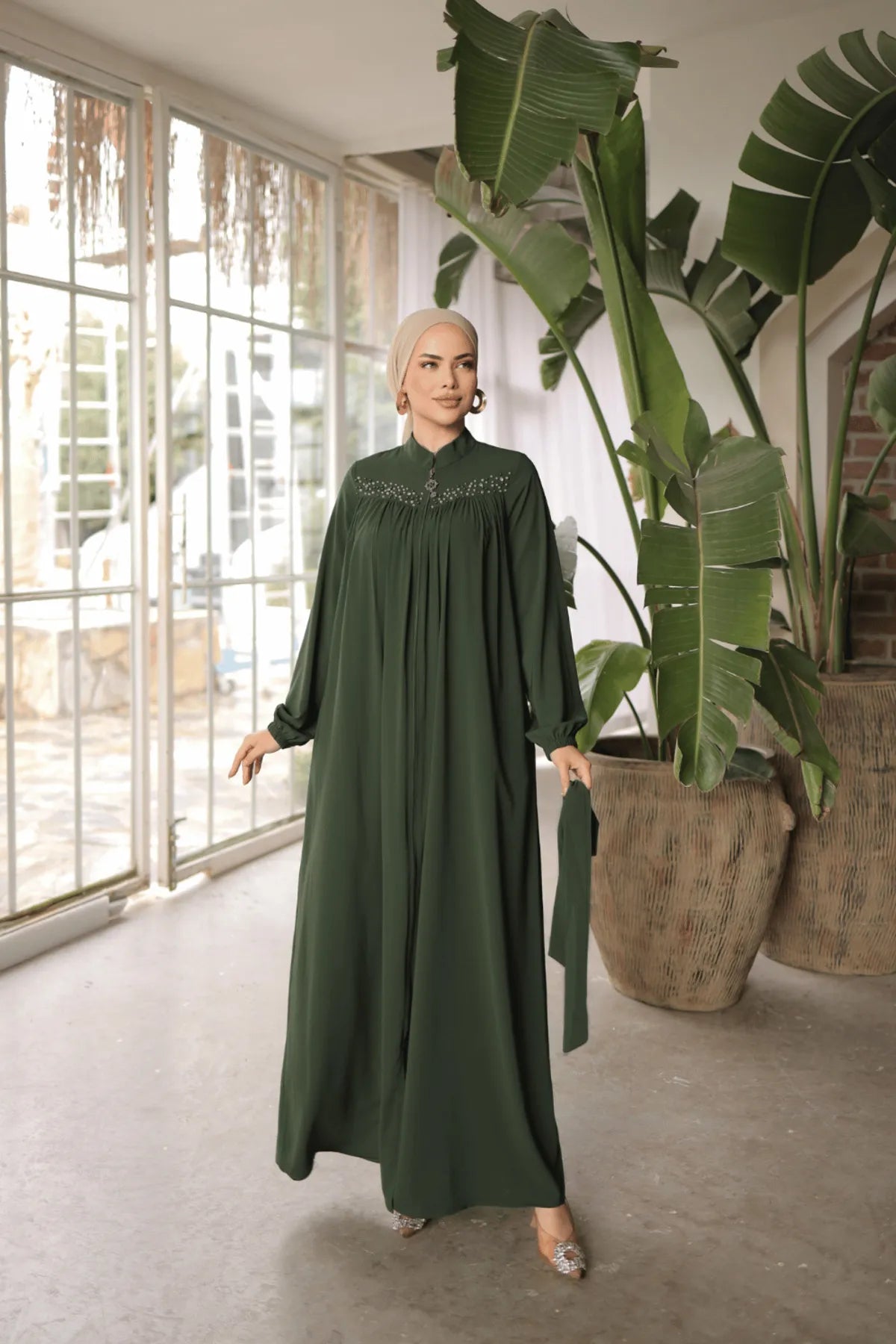 Chic green abaya featuring side pockets, a front zipper closure, and matching waist belt for a flattering fit. Embellished with pearls on the upper chest.
