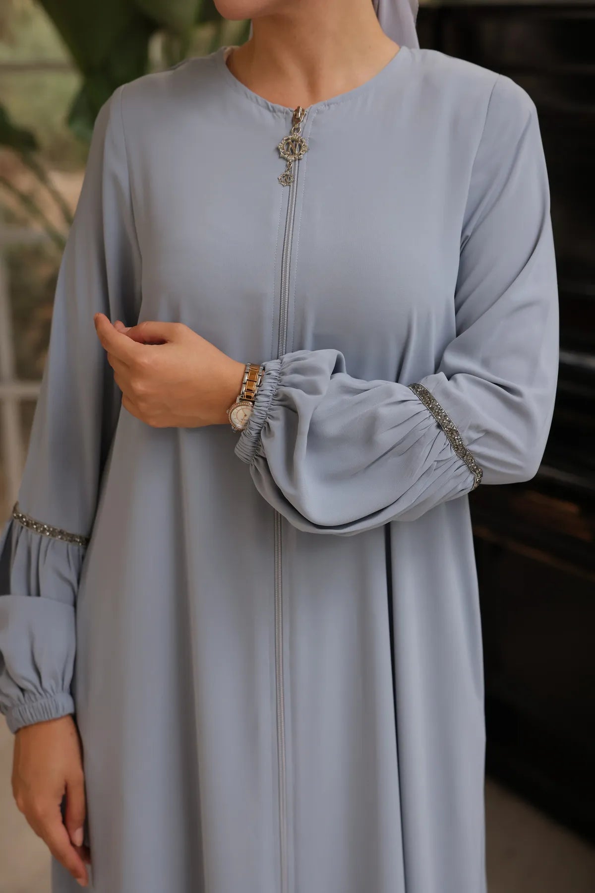 Close up, woman wearing a zipper-front abaya with elegant puff sleeves, a flowing silhouette, side pockets, and a modest fit, paired with a matching hijab and embellished flats.