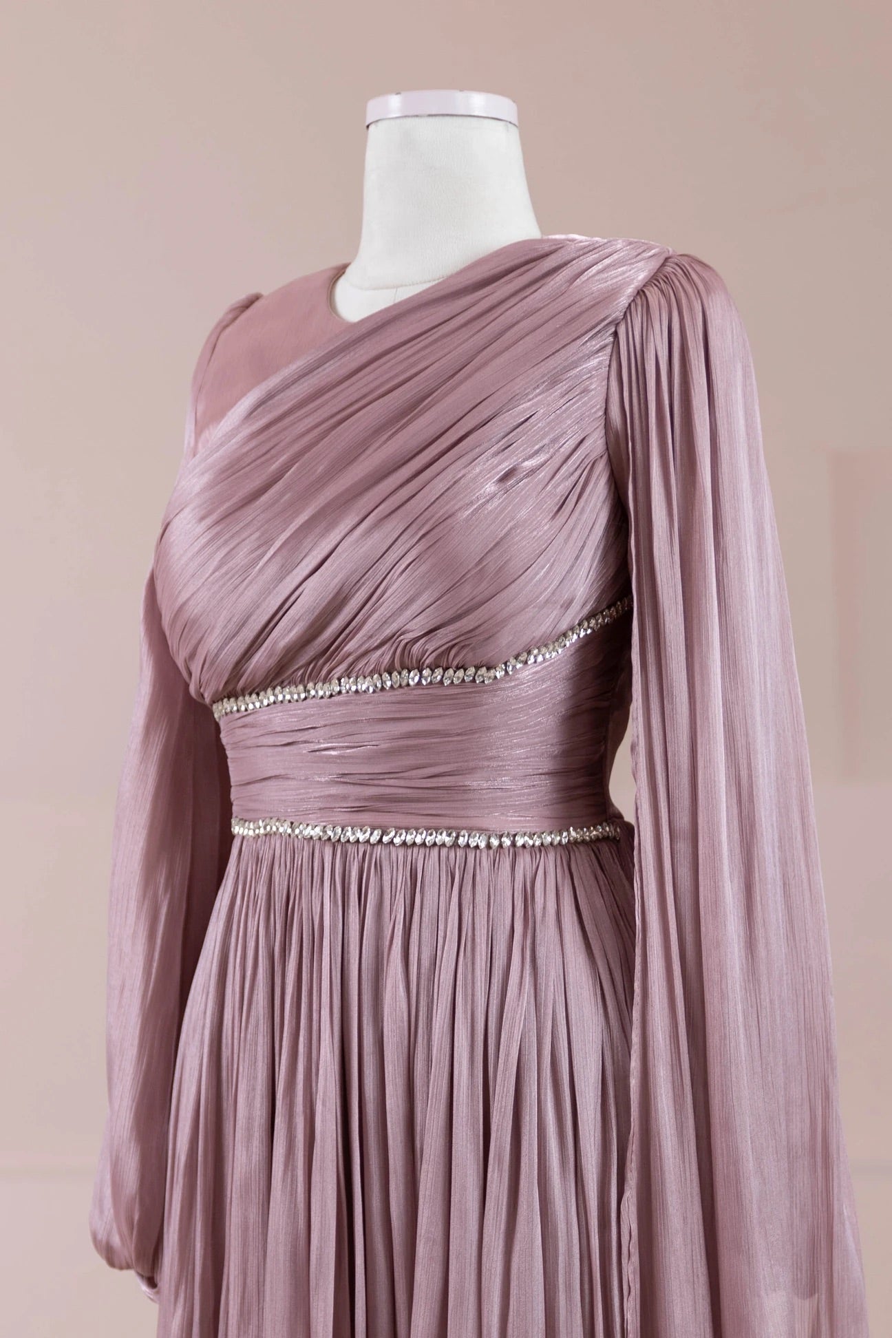 Close-up of dusty rose pleated maxi dress with long sleeves and crystal waistband accents