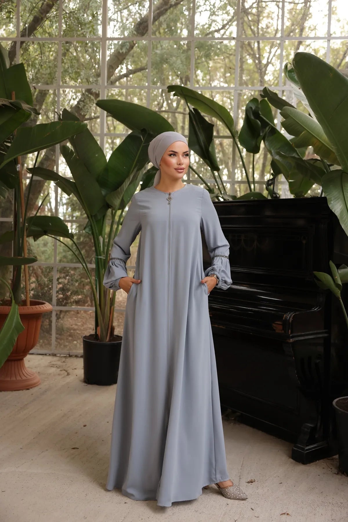  woman wearing a zipper-front abaya with elegant puff sleeves, a flowing silhouette, side pockets, and a modest fit, paired with a matching hijab and embellished flats.
